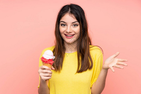 青红头发的年轻女人拿着一个玉米角冰淇淋在孤立的粉红色背景和惊吓图片
