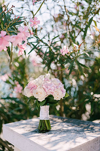 新娘花束玫瑰和奶油玫瑰和马蹄莲在盛开的玫瑰夹竹桃灌木附近的白色石铁路图片