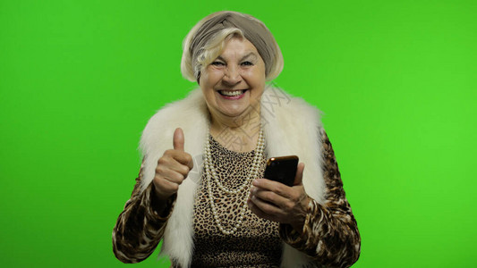 老年时尚老奶白种人成熟女使用智能手机上的应用程序成功在线购物色度键背景穿着时尚的老奶在手机上浏图片