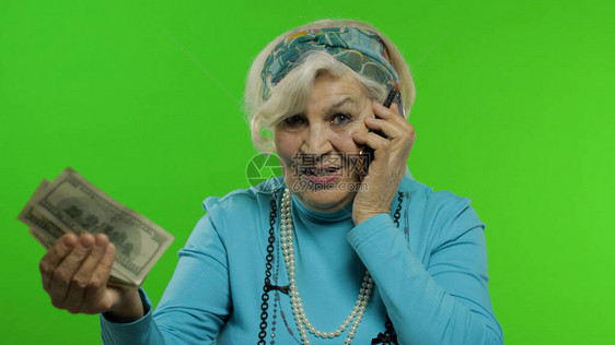 老年时尚老奶白种人成熟女人在手机上情绪化地交谈并展示钞票色度键背景有智能手机的老祖母在时尚衣图片
