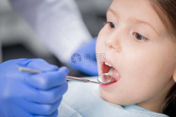 专业牙医用牙镜检查小女孩嘴巴张开的牙齿时戴手套的手图片