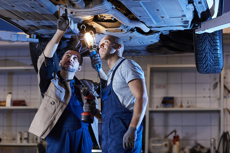 两名机械师站在汽车维修车间电梯下检查车辆的戏剧肖图片