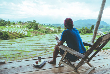 亚洲人旅行自然旅行放松坐在度假村的阳台上看书山上田野的景色笔记本电脑图片