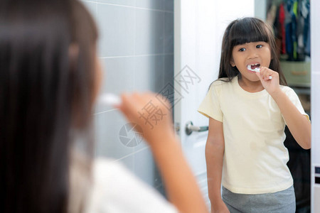 可爱的亚洲小学女孩在家里的浴室里刷牙和照镜子为上学做准备的生活中一天的图片