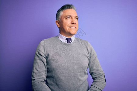 穿着优雅的毛衣和紫色背景的中年长相英俊的灰发男子在脸上微笑图片
