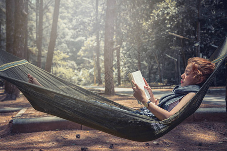 女人睡在吊床上看书在公园的自然大气图片