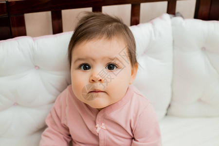 穿着粉色袖子的可爱小女孩在她的木制婴儿床图片