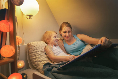 母亲和女儿在家睡觉前晚上一起阅读童话尾巴小说图片