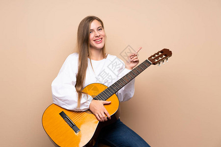 带着吉他背着孤立背景的青少年女孩指向另一边图片