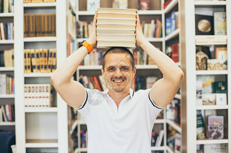 微笑的男人在图书馆里头顶着很多书成人和年轻图片