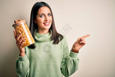 棕色孤立背景上拿着干意大利通心粉的黑发年轻女人非常快乐地用手和图片