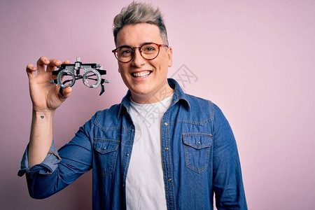 年轻的现代光学验光师男子在粉红色背景上拿着验光眼镜图片