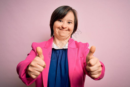 在粉红背景成功之后的年轻综合症女商人做了正面的手势笑着图片
