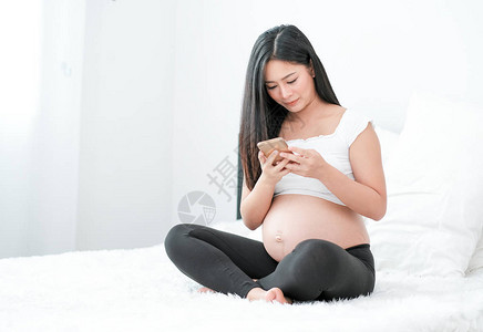 亚洲漂亮的孕妇用她的手机查看一些关于从互联网上搜索婴儿护图片