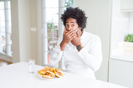 非裔美国人饥饿的人吃汉堡吃午餐时会因错误而用双手遮住嘴秘密概图片