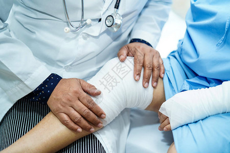 亚洲老年或老年妇女患者在护理医院病房的床上用绷带包扎膝盖意外背景图片
