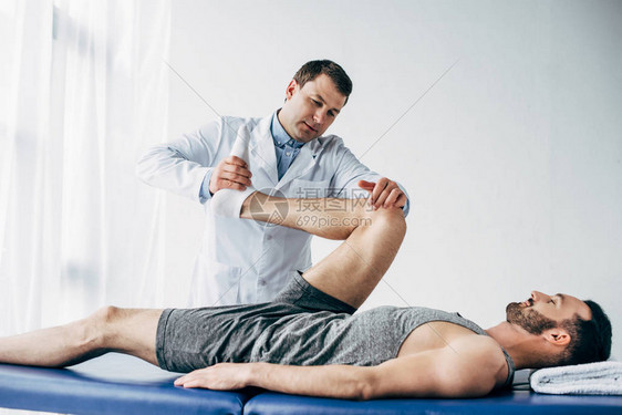英俊的脊医在院伸展病人的腿图片