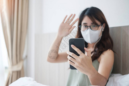 在家戴口罩和通过智能手机进行视频通话的休闲病女图片