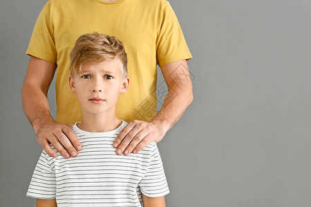 父亲在灰色背景下将害怕的儿子的双手放在肩膀上图片