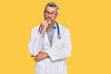 中年白发男子穿着医生制服和听诊器严肃的脸用手放在下巴上思考问题图片
