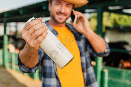 农民有选择地重点谈论智能手机和在看相机时持有一瓶新鲜牛图片