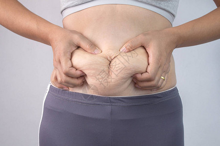 女人的手在灰色背景下捏住过多的腹部脂肪的特写镜头女人肥肚子肥胖图片