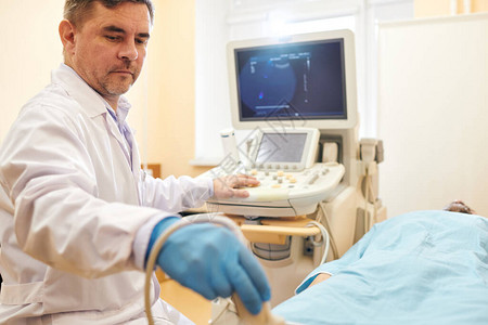 在对住院病人进行超声波检查时使用检测器的实验室大衣严背景图片