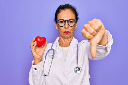中年高级心脏病专家医生女在紫色背景上拿着红心图片