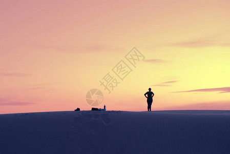 探索者的女人从沙丘上俯视沙漠在日落时正对图片