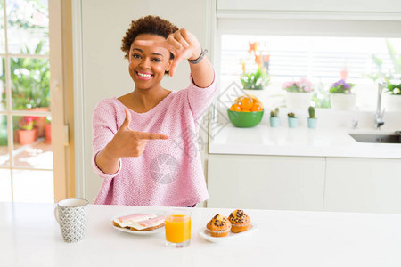 早上在家吃早餐的年轻非裔美国妇女微笑地用手和指做架子图片