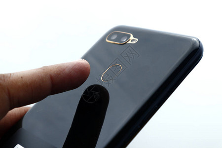 在有白色背景的智能手机后面的指纹扫描仪上贴近人类手指照图片