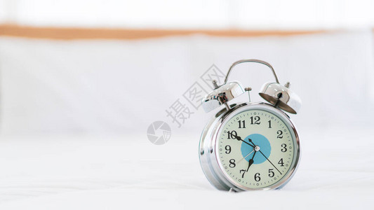 白色床上的复古风格模拟闹钟与copyspace密切相关早上睡觉和疲惫的工作人员几乎7点的图片