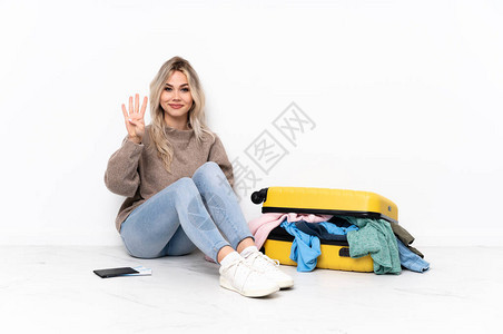 年轻金发女孩带着一箱装满衣服的手提箱坐在地板图片