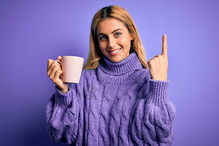 年轻漂亮的金发女郎在孤立的紫色背景中喝着咖啡图片