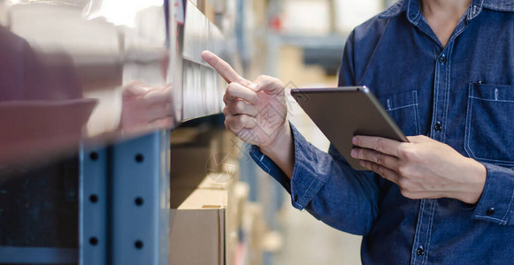 亚洲经理人使用平板电脑在仓库货架上的纸板箱中对产品管理进行盘点背景图片