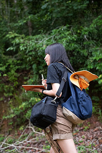 美丽的女人背着包手拿书在公园里行走图片