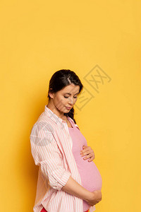 黑发孕妇站在黄色上摸肚子背景图片