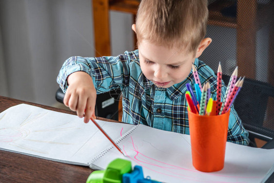 可爱的孩子在桌子上的相册里用铅笔在纸上画学前教育的概念与图片