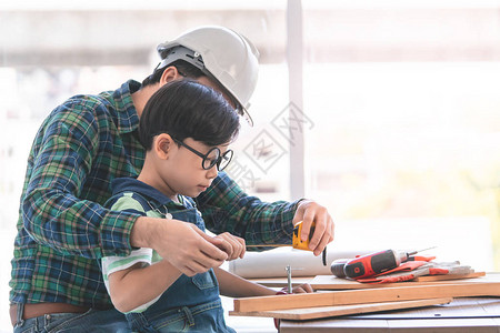 小男孩正在学习木柴上做工并且从他的手工艺人父亲那图片
