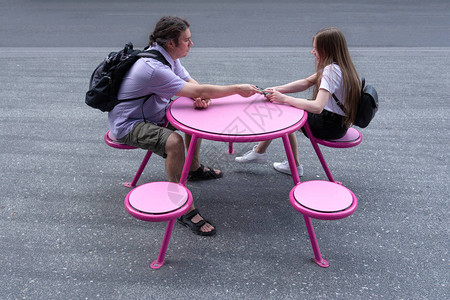 一个年轻的男人和一个女孩坐在街上的一张粉红色的桌子旁一个男人正试图接一个女孩的电话关系图片