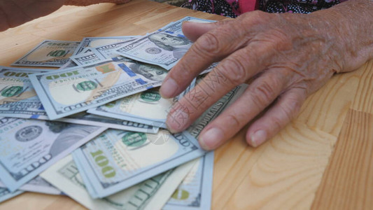 祖母怀里从桌子上扫出一捆散落的百元钞票皱巴的女手从桌子上拿出一堆的外币顶背景图片