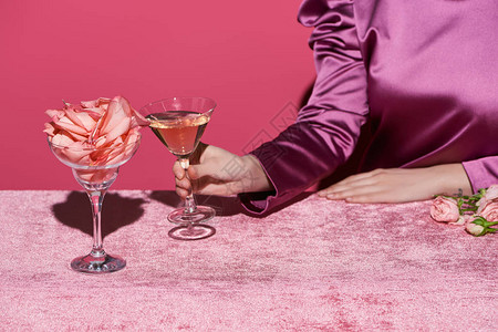 女在玻璃附近举着玫瑰酒杯与丝绒布上玫瑰花瓣图片