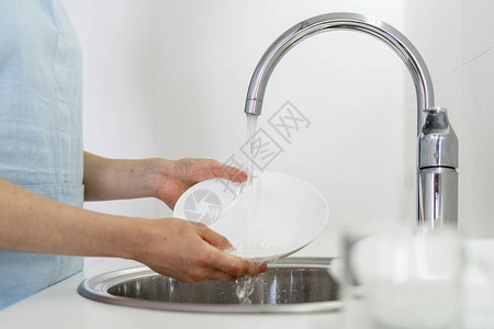 妇女用手拿着餐具在水槽下洗盘子站在白色明亮厨房图片