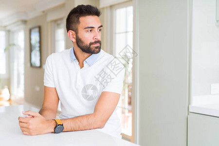 英俊的西班牙裔男士休闲白色T恤在家里看着一边图片