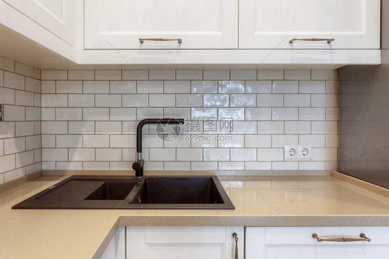 现代公寓与现代内饰在厨房与白色橱柜和墙上的瓷砖石台面上带黑色水龙头和图片