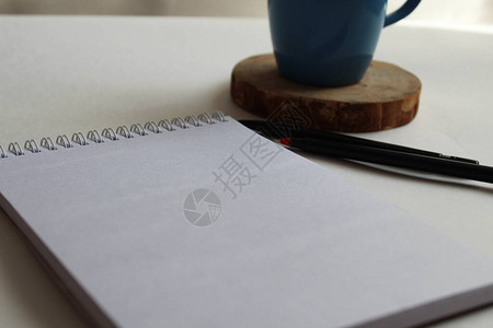 桌子上有一张白纸旁边是用来写字的记事本杯子碟子绿色红色或蓝色有一个地方可以插图片