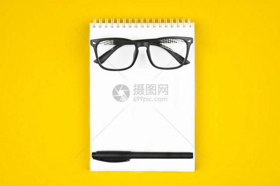 黑色眼镜笔记本上的钢笔黄色背景图片