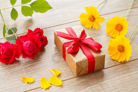 装有红玫瑰和黄花的木板上的红丝带包起来的礼品图片
