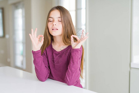 白桌上的漂亮年轻女孩放松闭上眼睛微笑用手指做冥想手势图片