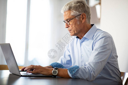 使用膝上型计算机坐在办公桌的戴眼镜的背景图片